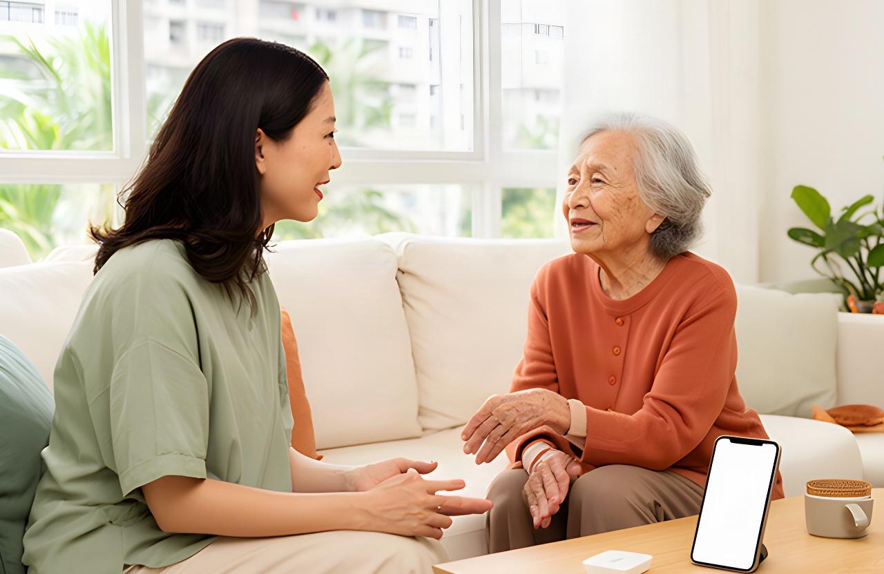 Adult daughter speaking with her elderly mother in a bright Singapore HDB living room, with a phone resting on the table